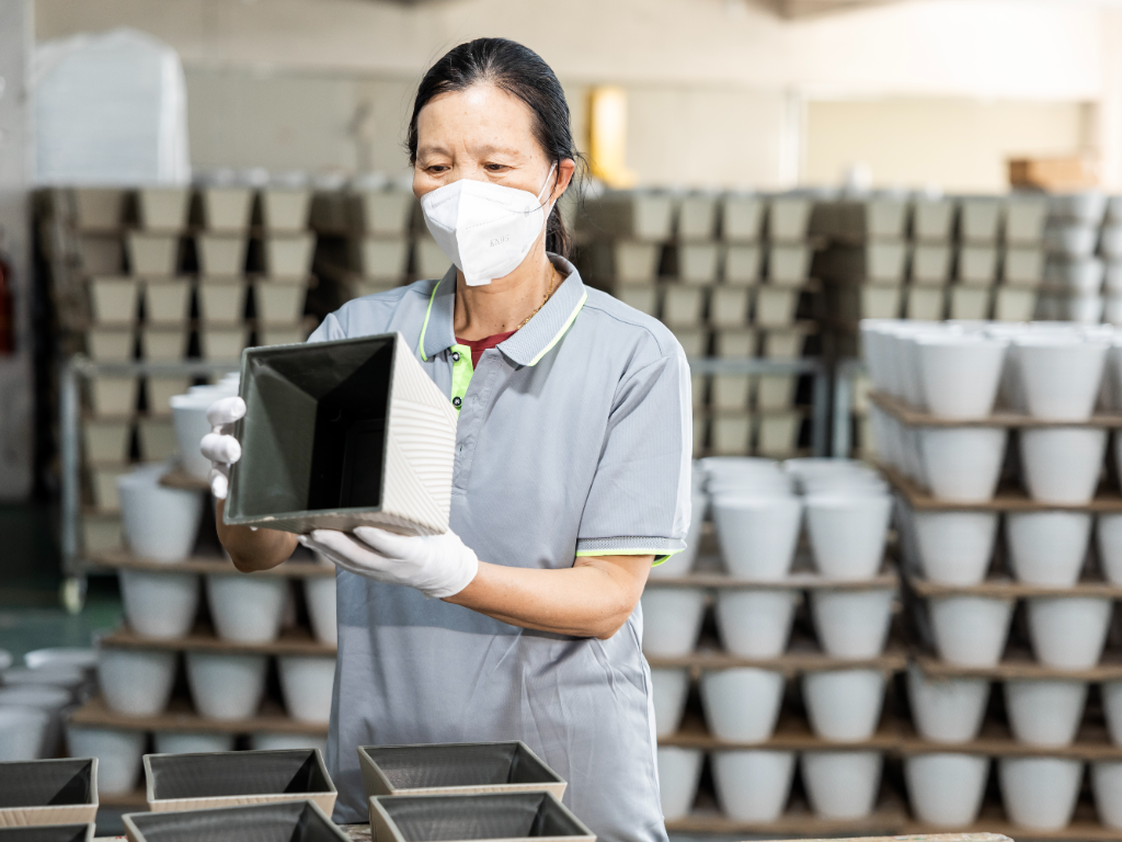 A factory worker inspects a newly patterned plastic flower pot.