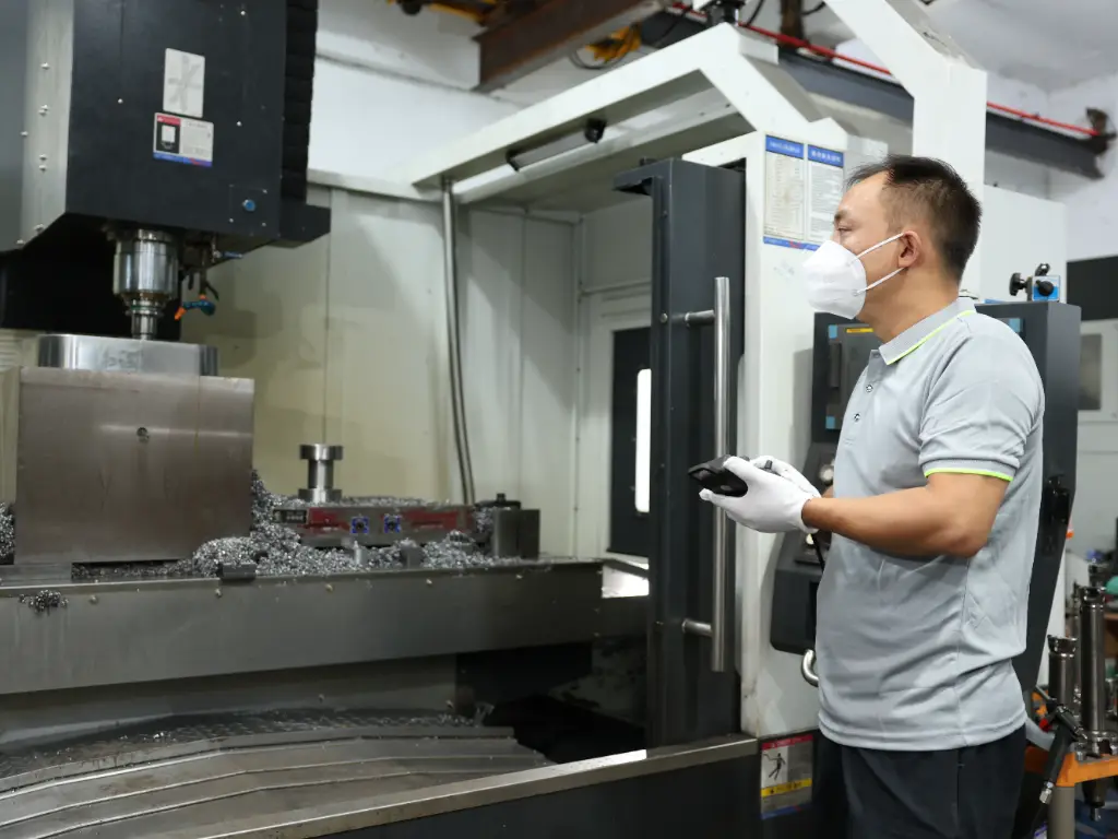 A technician in a mask and gloves operates a CNC machine used for making moulds.
