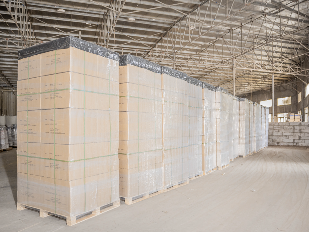 Large stacks of shrink-wrapped boxes on pallets in a warehouse.