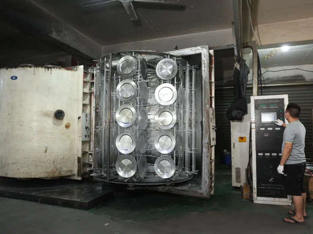 A worker operates a large plating machine filled with saucers.