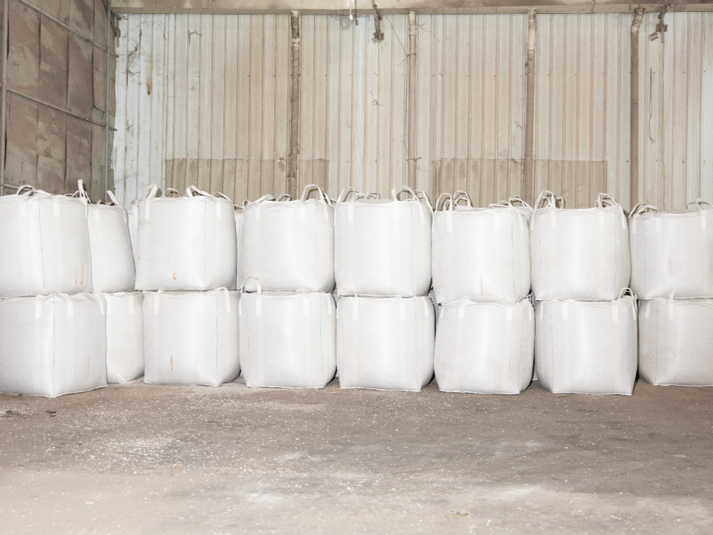 Large white bags of raw materials stacked in a warehouse.