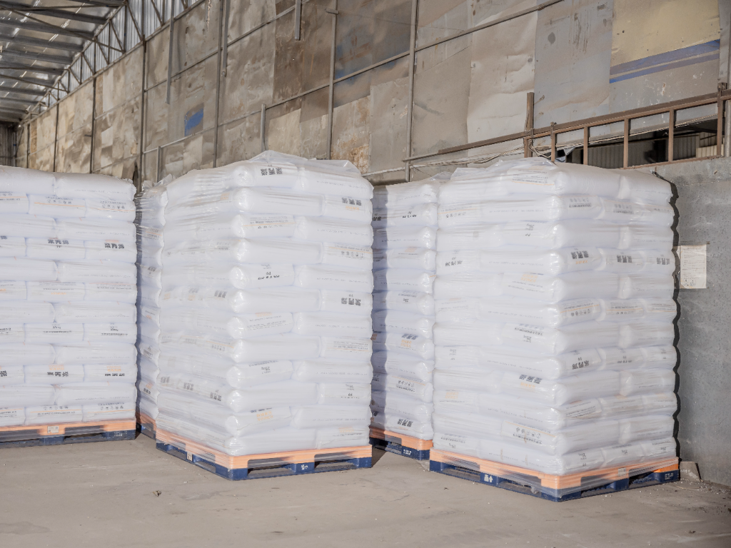 Large bags of recycled PP plastic pellets on pallets in a clean warehouse.