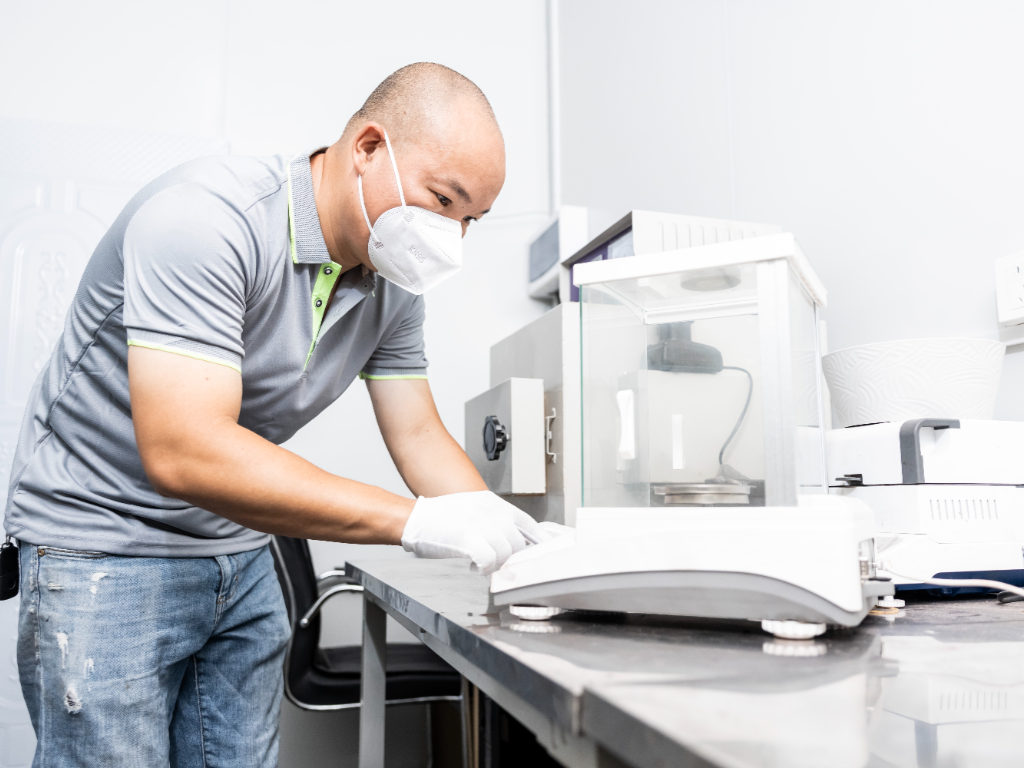 A lab technician in a mask and gloves conducts a test on raw materials.