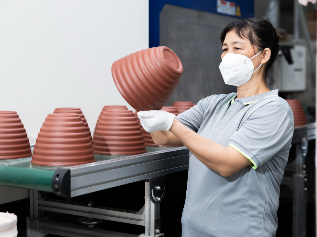 A factory worker in a mask and gloves holds a newly made plastic flower pot.
