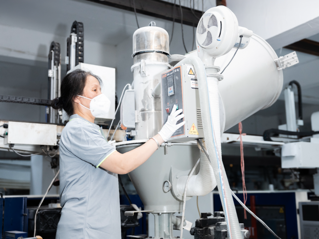 A factory worker in a mask and gloves operates a machine.
