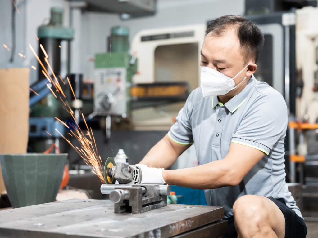 A factory worker uses a CNC machine to grind a mold, creating sparks.