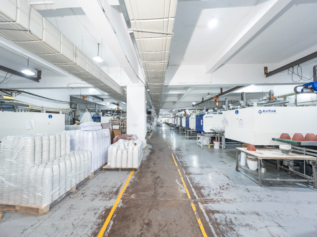 A long, organized production line with several injection molding machines and stacked products in a clean factory.
