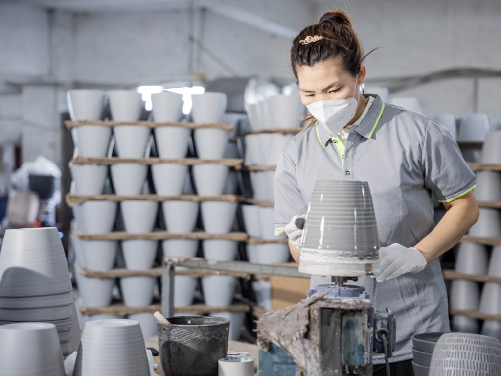 A close-up of a factory worker sandblasting a plastic flower pot, creating a textured surface.